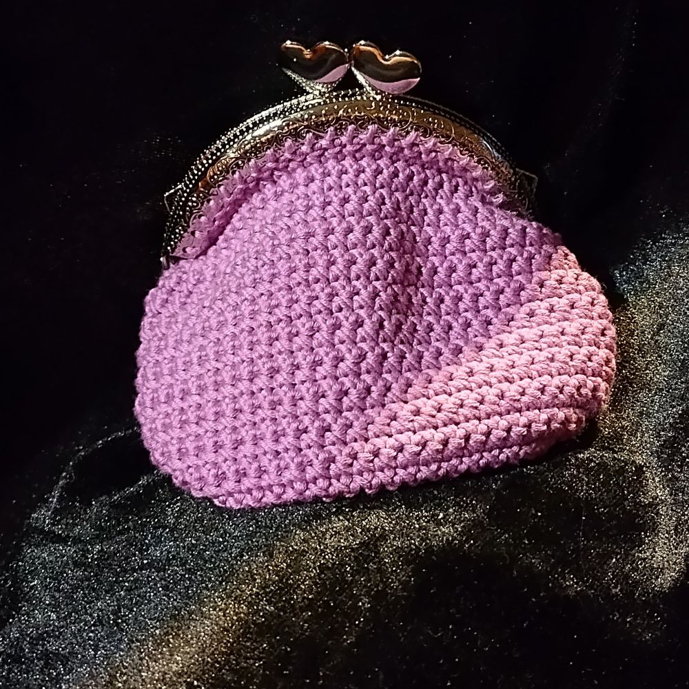 A light purple, crocheted purse with a silver clasp, clasp has two hearts to fasten.