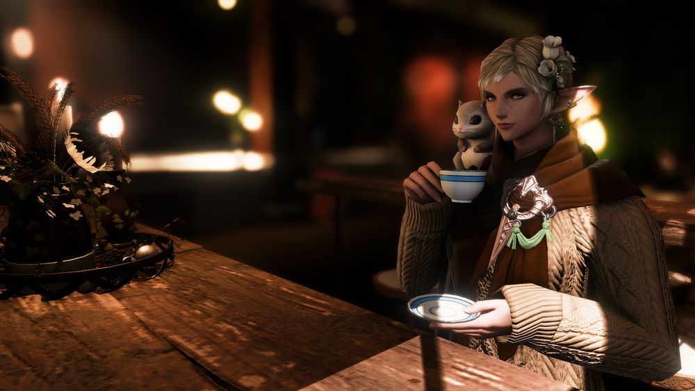 Divi is drinking some tea at a local cafe, at a table next to a window, with Cashew on her shoulder.