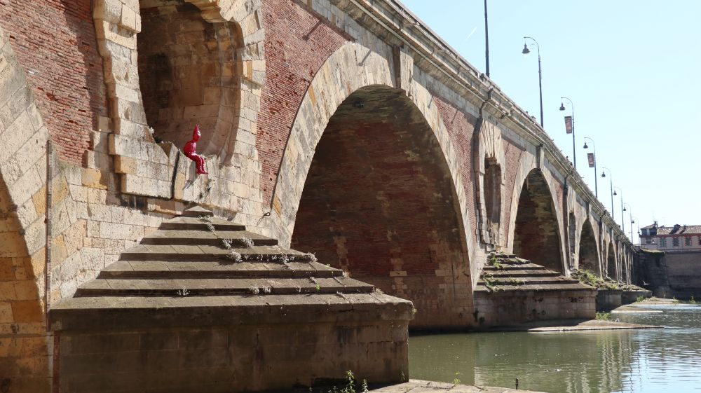 Pont Neuf in Toulouse. A sculpture of a red child sits under one of the arches in the foreground.