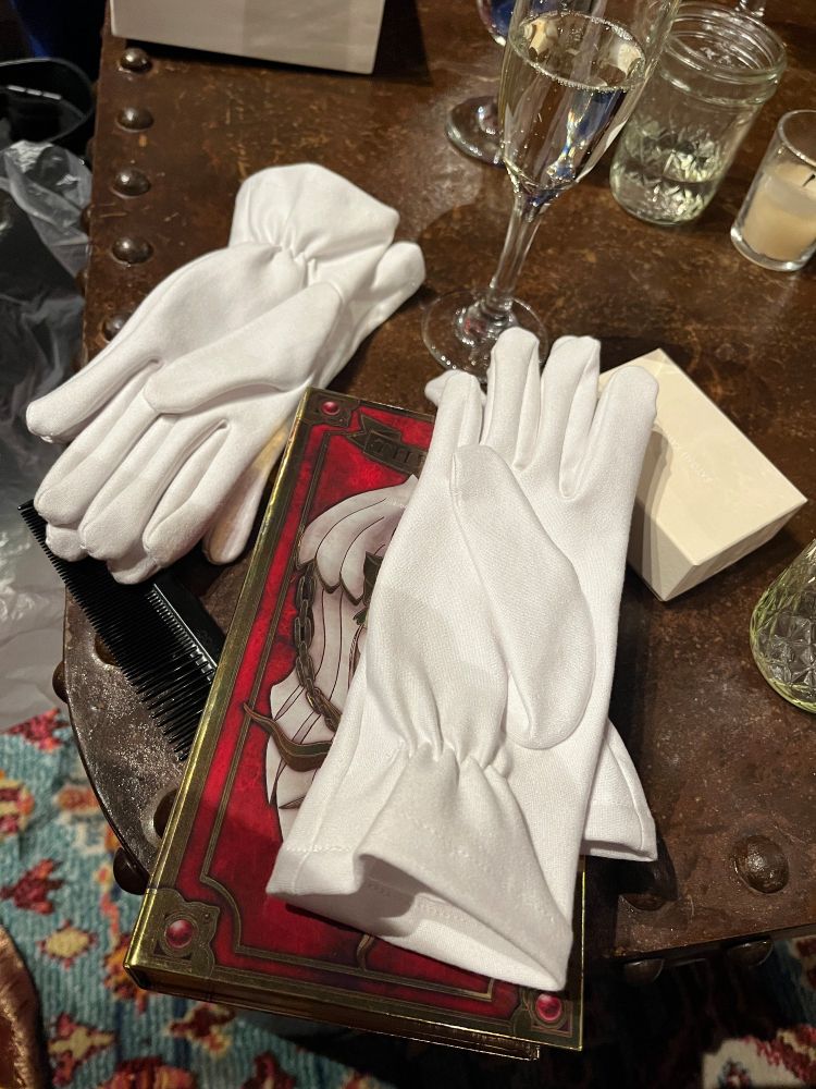 Two pairs of white gloves sitting on a table, over the Book of Clow