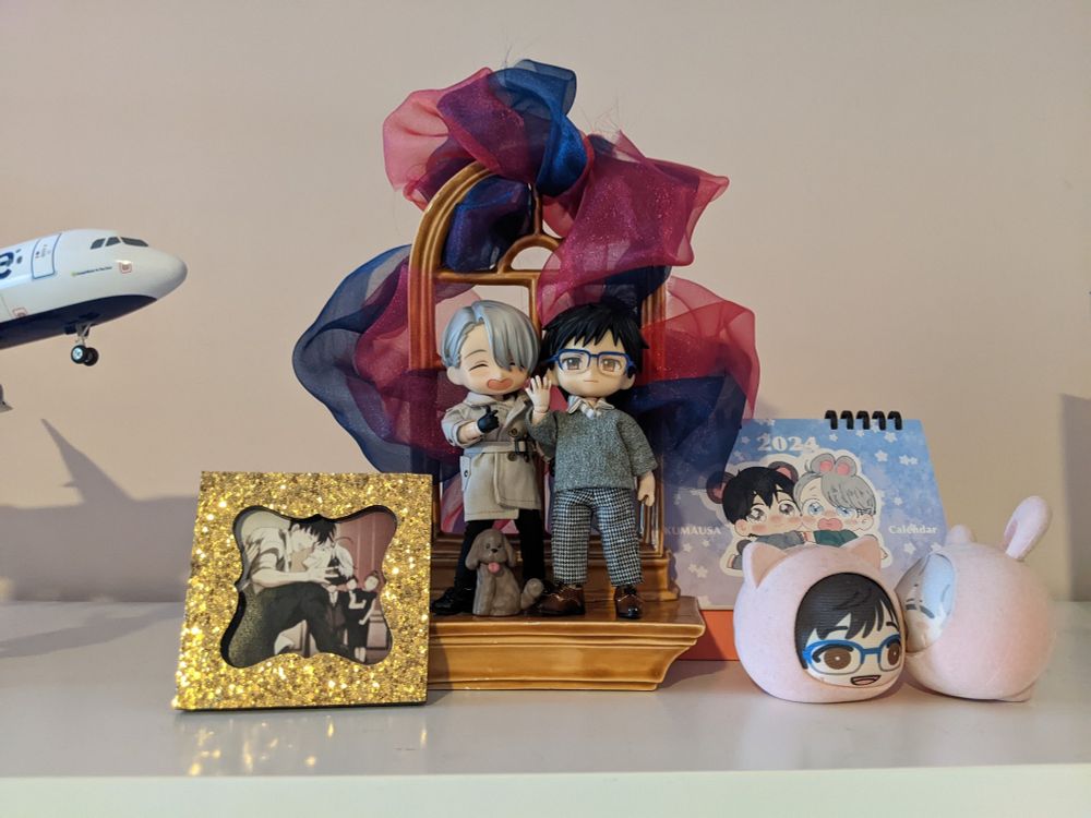 Victor and Yuri nendoroid/obitsu dolls posed with their rings showing, surrounded by other YOI merch