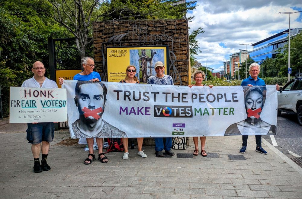MVM Northwest Surrey local group outside Woking's Lightbox Gallery - holding a huge 'Trust the People - Make Votes Matter' banner and getting honks from passing traffic in response to a 'Honk for Fair Votes' placard.