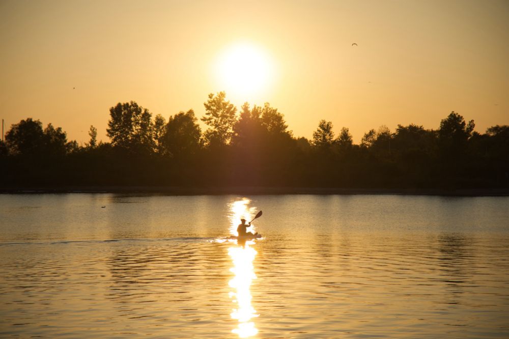 Sunset on a lake, with a silhouette of a person kayaking, golden hour