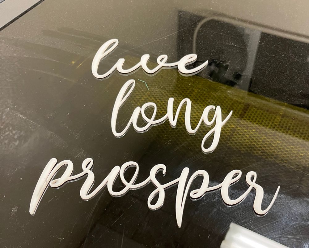 Three words laser-cut in milky white acrylic. The words read “Live” “Long” “Prosper” in a whimsical cursive hand.