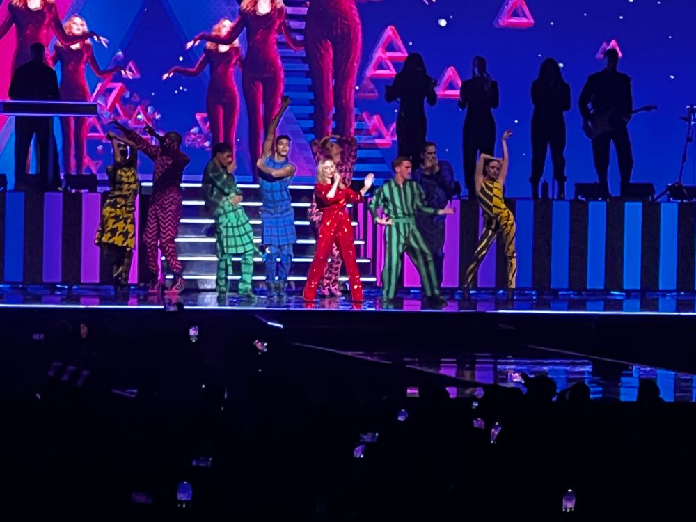 Kylie with an array of dancers behind her in brightly colored outfits 