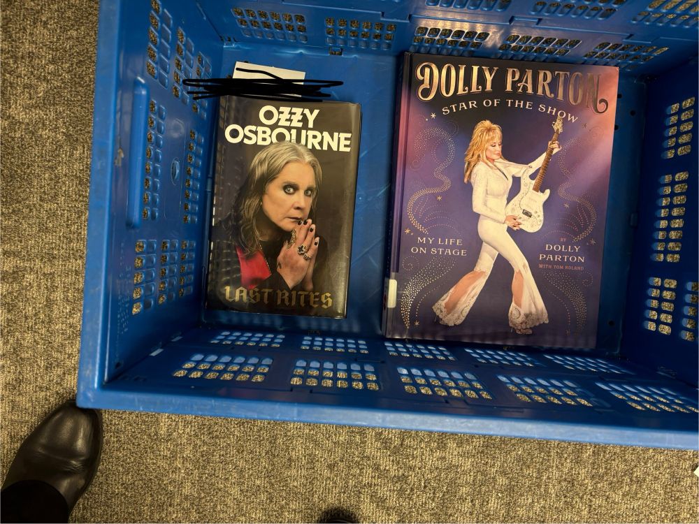 A blue plastic book crate containing biographies of Ozzy Osbourne and Dolly Parton.