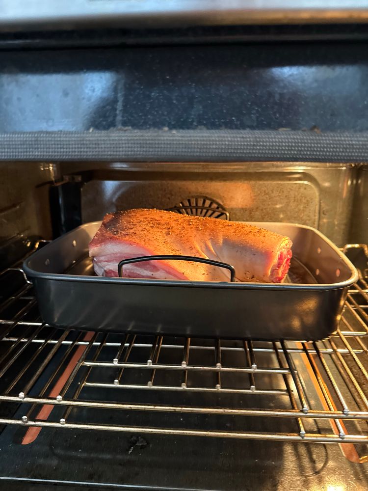 A pork shoulder in a roasting pan in an oven after 2h of cooking