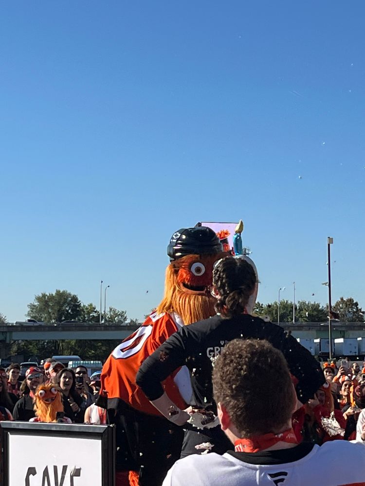 Gritty rises up as he begins to take his swing, cake in hand. His right eye is higher and more obvious that in prior picture. The volunteer/victim in the foreground remains arms akimbo. 2/3