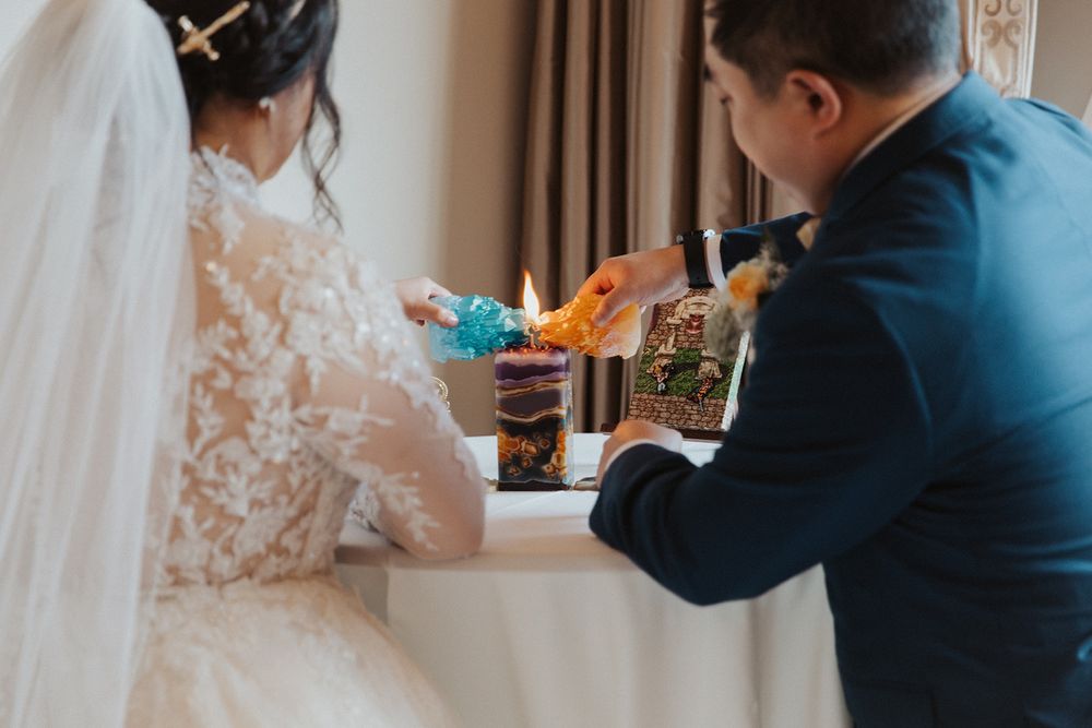 A photo from behind my husband and me lighting a unity candle that looks like a rock formation, with me holding a blue candle that looks like a gemstone and my husband holding an orange candle that also looks like a gemstone, with the flames of our candles uniting. A canvas of a game screenshot of Chrono and Marle underneath Leene's Bell is on the table behind the unity candle.