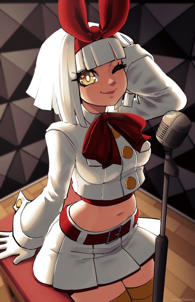 A woman with white hair sits on a stool in a sound booth with a microphone in front of her. She has her large red bow in her hair and is wearing a white cropped jacket and pleated white skirt with red accents. She has white gloves and a large red ribbon around her neck. She is smiling at the viewer and has her left arm raised and running through her hair.