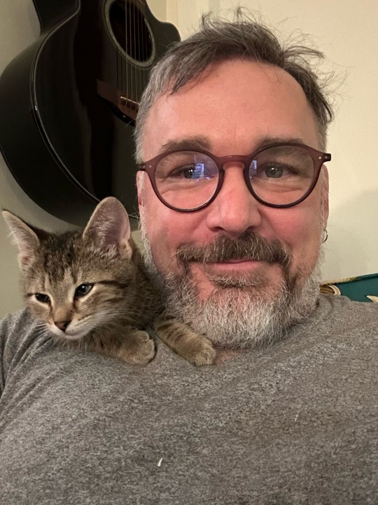Picture of a grey kitten sitting on an old man’s shoulder
