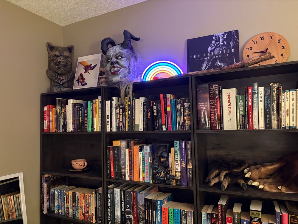 Bookshelves with a variety of stuff on top, including a Spirit foam werewolf bust, a femme Krampus mask, two large books, and an LED rainbow