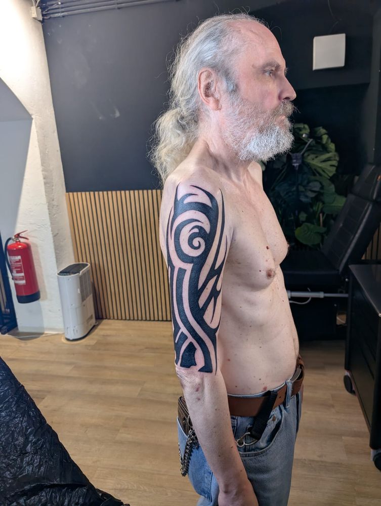 Ein Tribal Tattoo in schwarz am Oberarm eines grauhaarigen Mannes