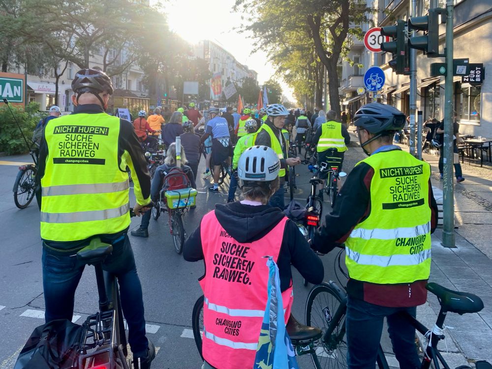 Am 15.09.25 stehen Teilnehmende der Demo Kantstraße auf der Fahrbahn, kurz vor dem Start. Im Vordergrund sind die Beschriftungen von drei Sicherheitswesten zu sehen: „Suche sicheren Radweg.“