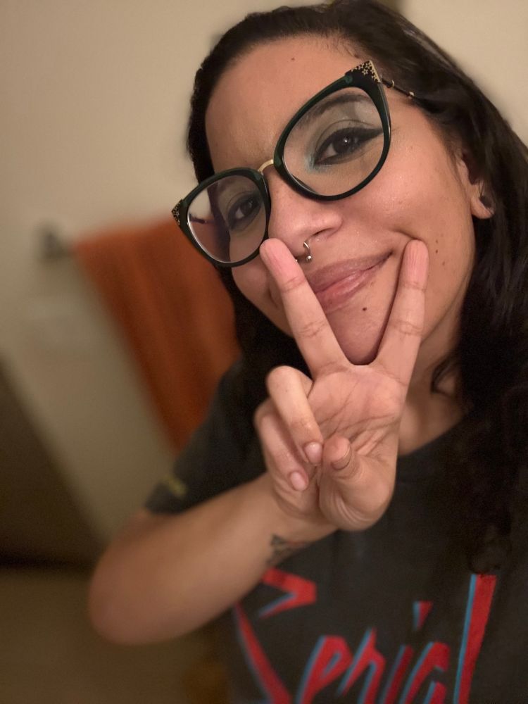 A Black woman in glasses holding up two fingers in a peace sign