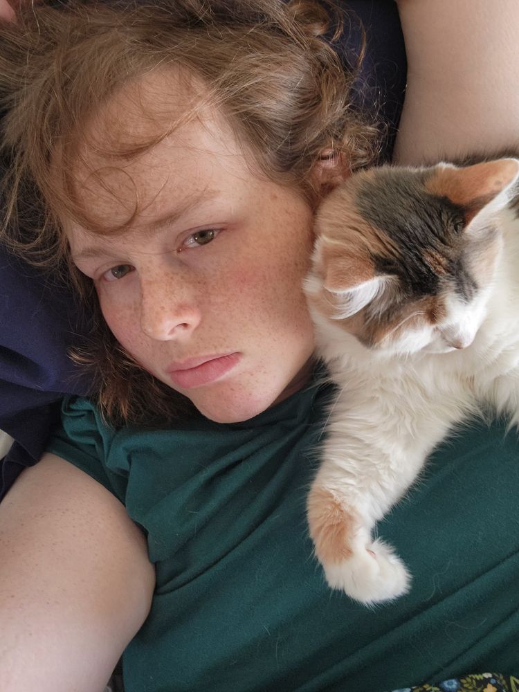 A selfie of myself and my cat with her resting her head against my face.