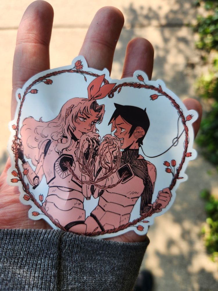 A sticker in my hand in which two women have one another's hearts in their hands ready to take a bite 