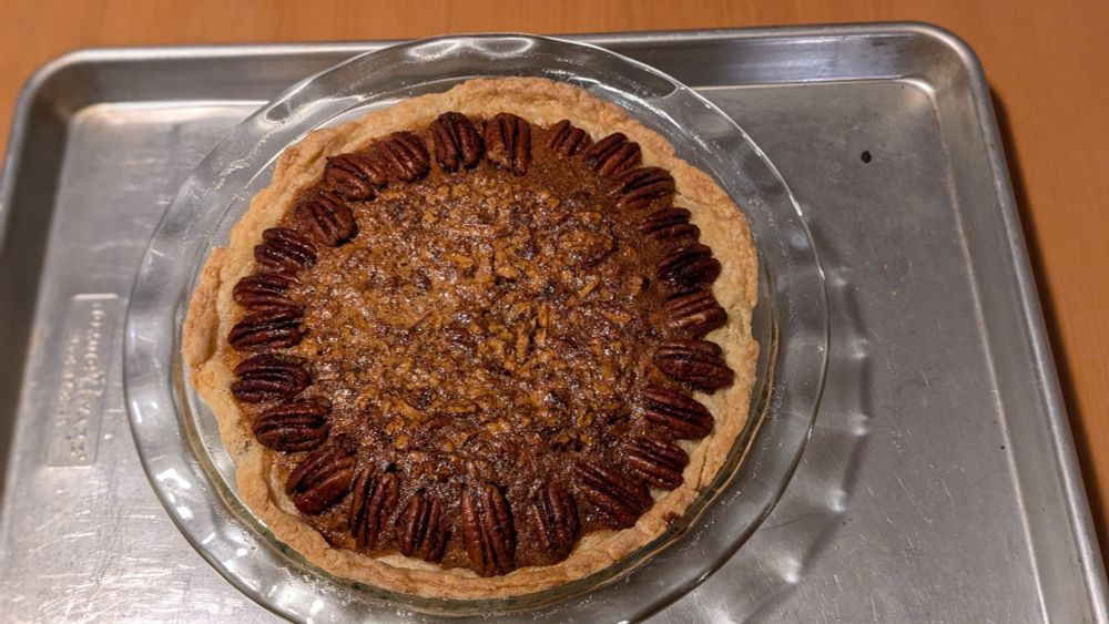 A pecan pie with a decorative ring of pecan halves at the edge of the crust, some of the pecans look burned but that's just our shit lighting in our dining room.