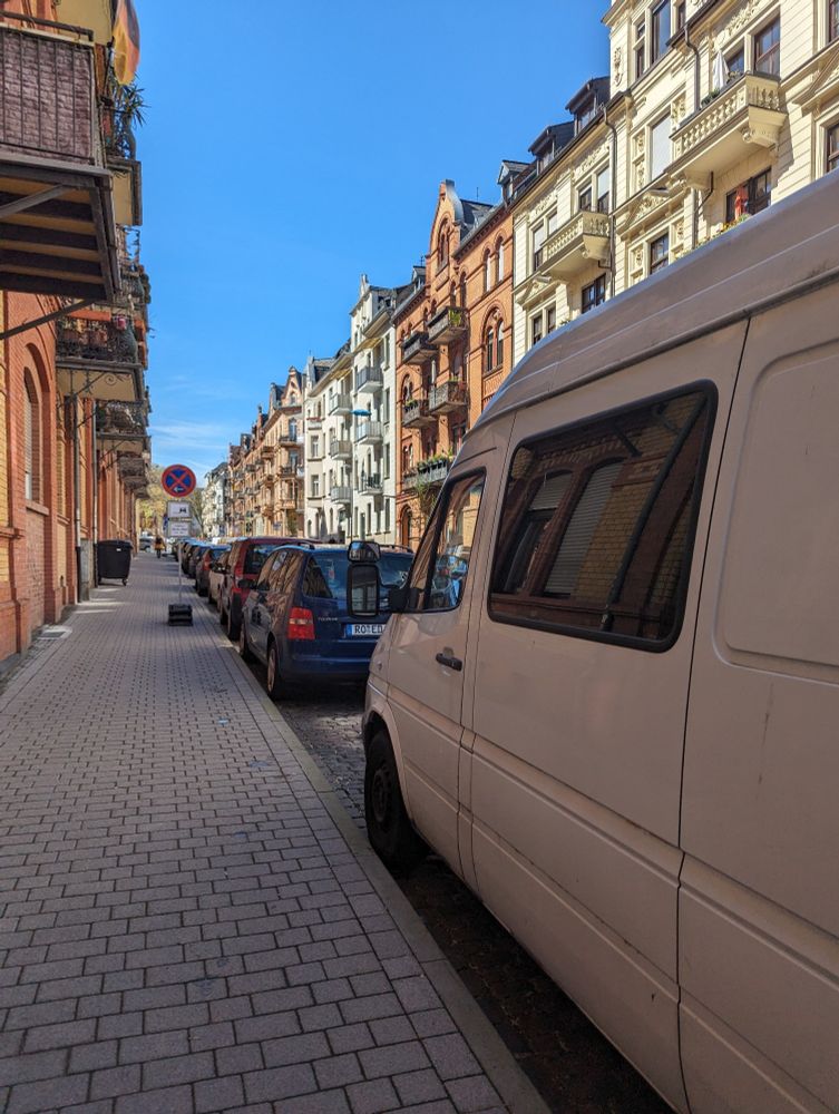 Foto vom Bürgersteig aus auf eine Straße. Der Blick ist nur nach vorne frei, in Richtung Straße wird die Sicht durch Parkende KFZ versperrt