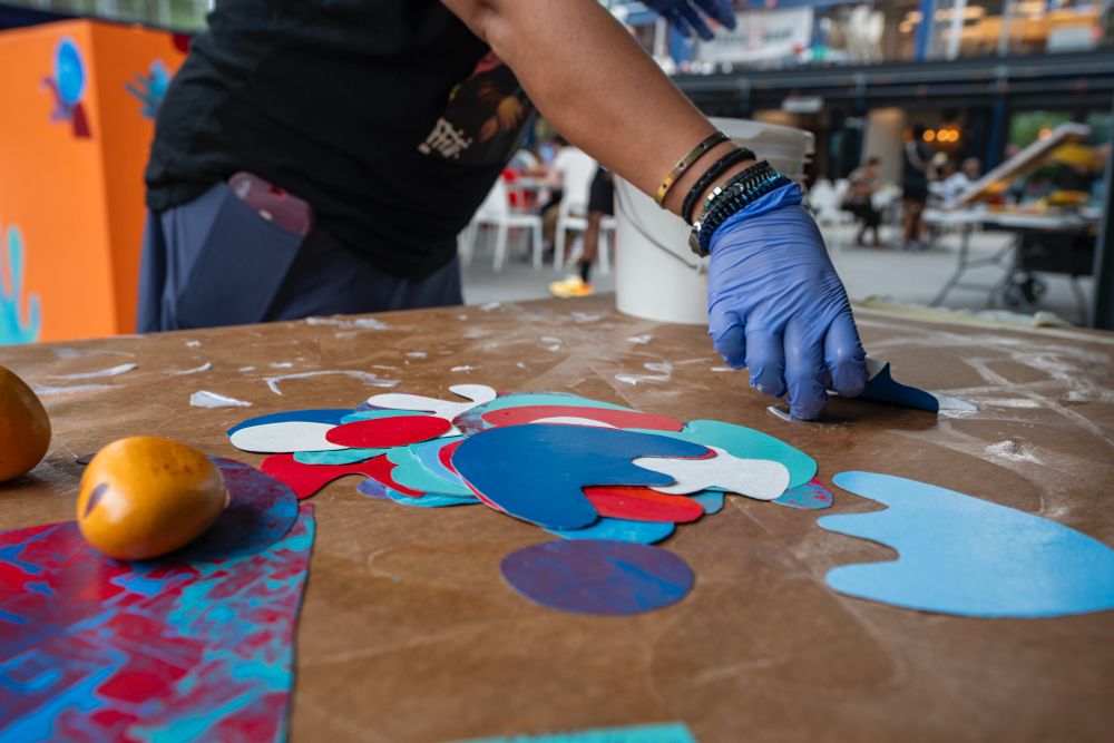 An artist prepares colorful pieces of PolyTab to be glued to an orange cube sculpture in a community collaborative project.