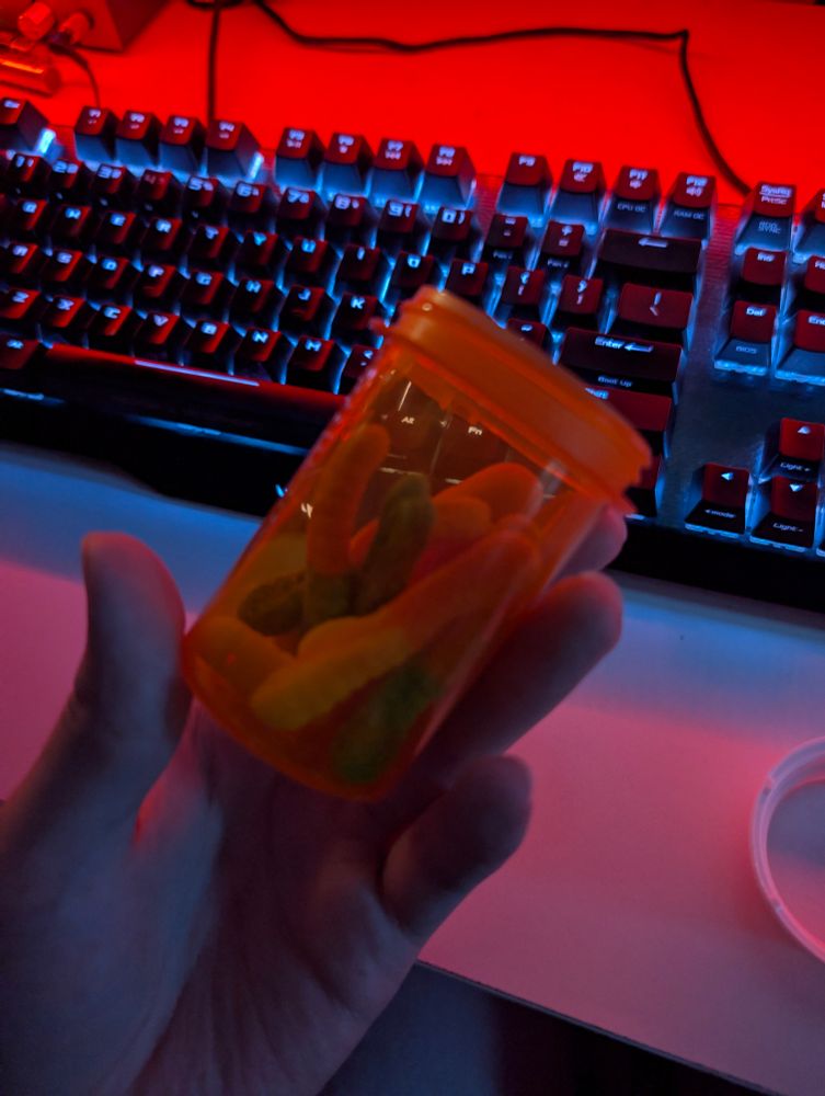 sour gummy worms in a large clear orange pill bottle, with the white twist cap off