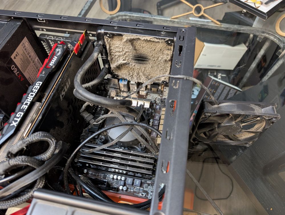 a desktop pc with the side open. there is a literal wall of dust caked on a radiator that was behind a now-removed fan that is sitting outside of the case