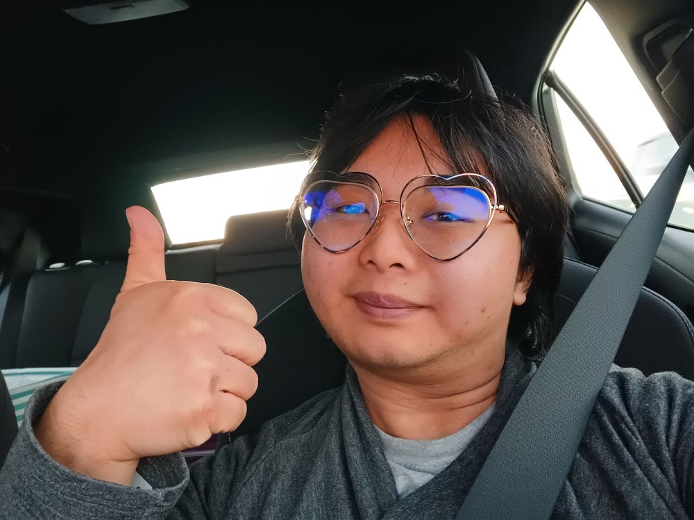 A photo of myself in a car, holding a thumbs up.