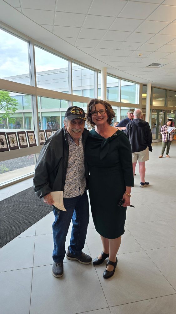 Man in Veterans hat and woman in green dress with a Gavel smile together 
