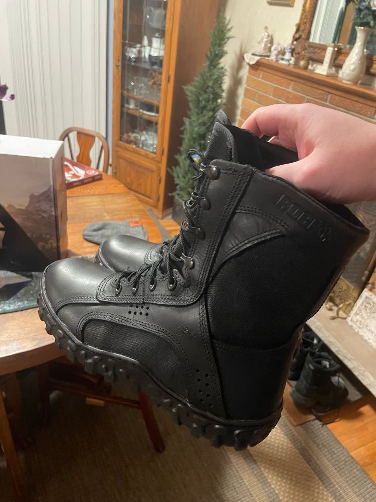 a pair of black combat-style boots in my hand, being held in the air