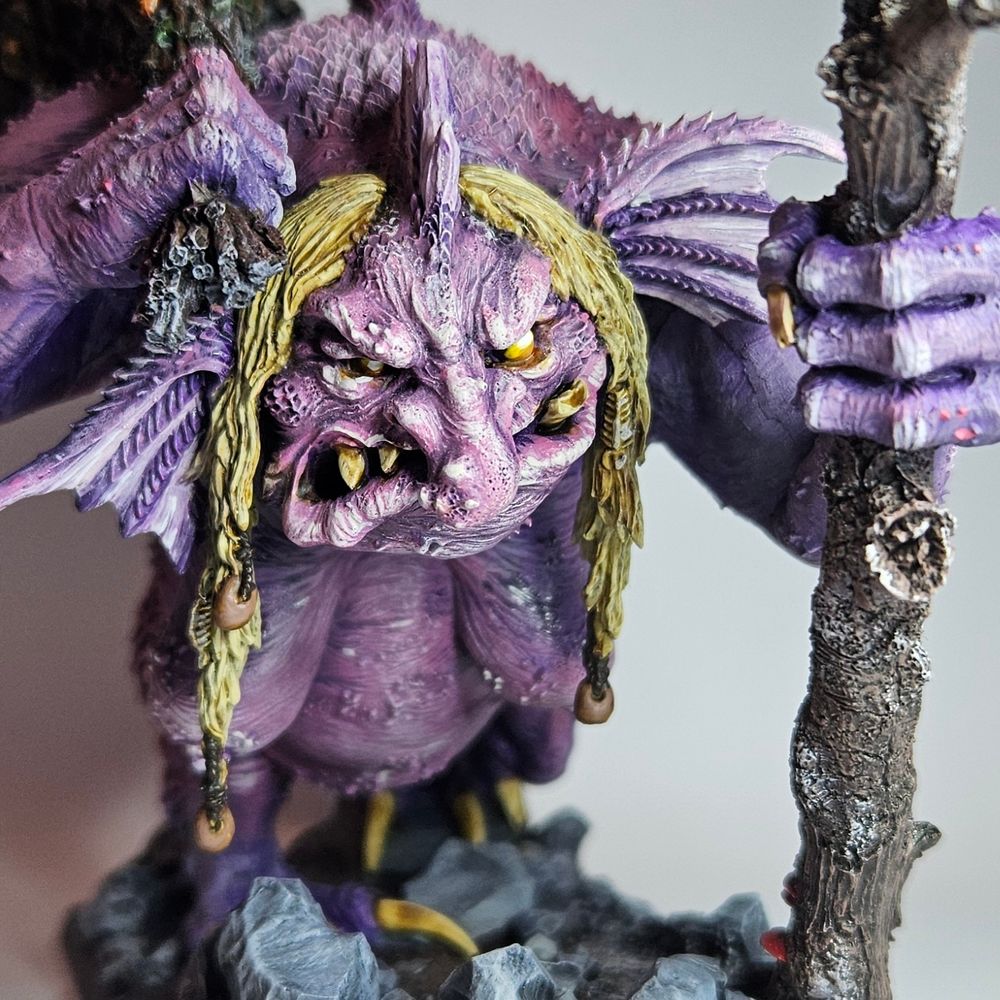 A warhammer old world Troll Hag in a walking pose, a close up of her face. Her skin is purple and pink, with dirty blonde hair. Her eyes are yellow, and her teeth are yellowing, she has a snarl on her face.