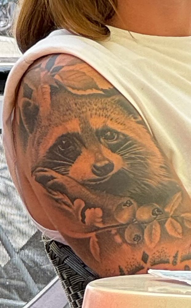 ein tattoo eines waschbären auf dem oberarm einer frau.