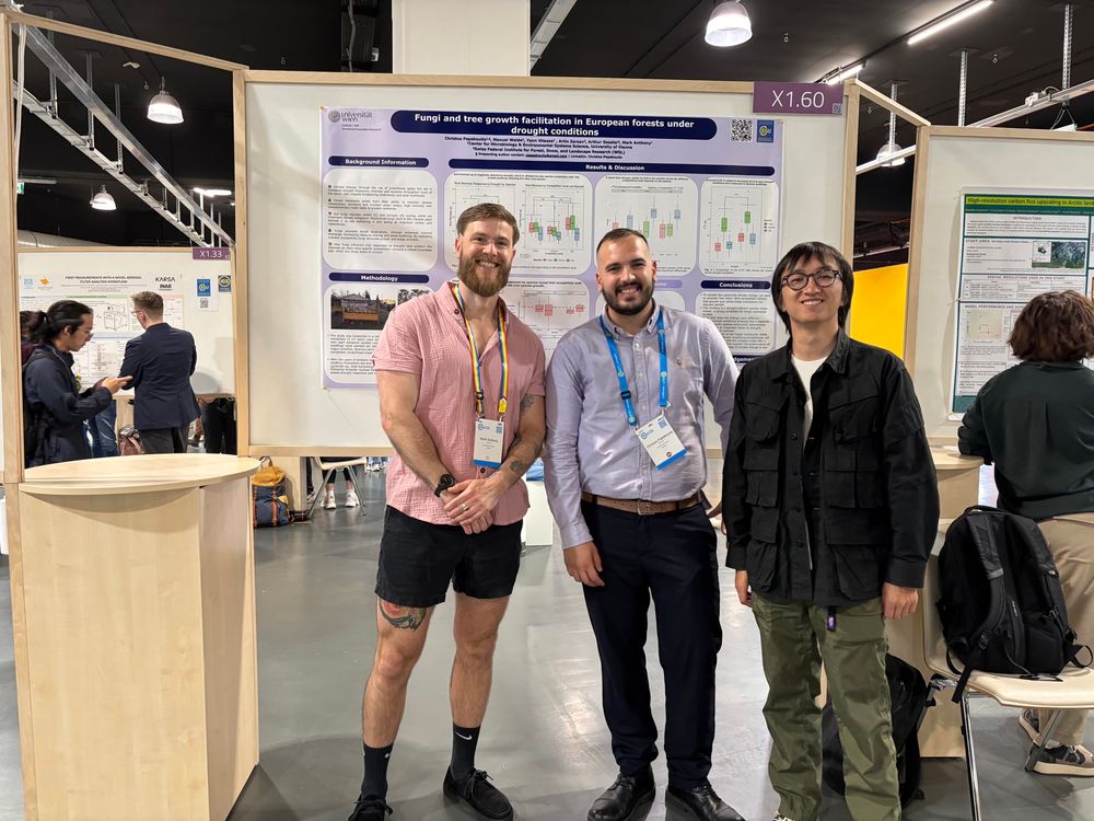 Three guys standing and smiling in front of a poster. 