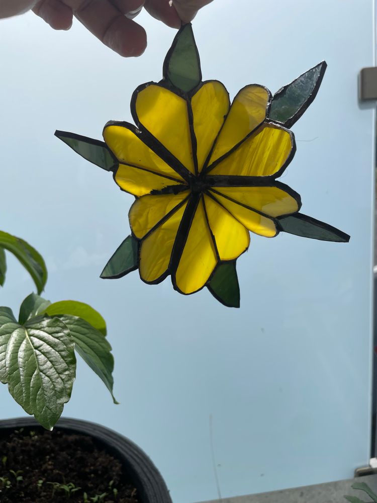 Gelbe Blume mit grünen Blättern aus Buntglas, verlötet mit Zink, schwarz patiniert 