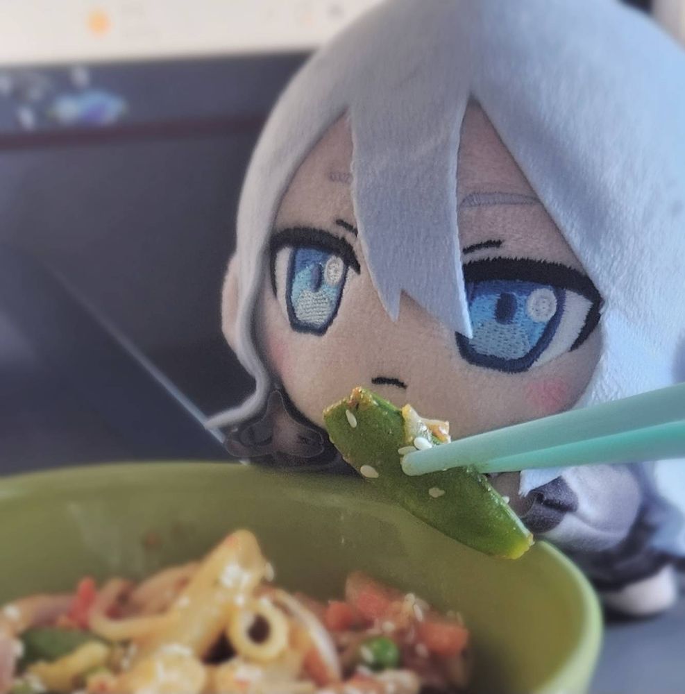 photo of yoisaki kanade nesoberi plush with a bowl of food. she is being handed a small piece of green bean