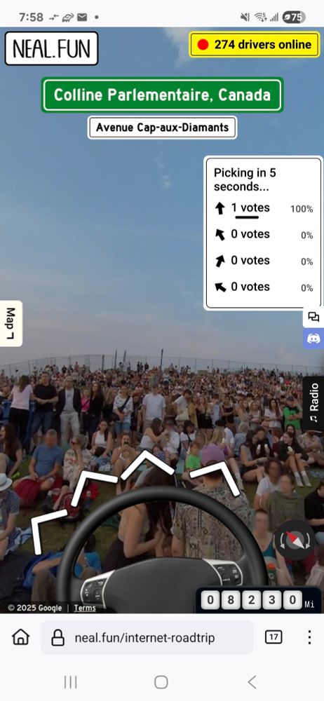 A car steering wheel superimposed over an image of a large gathering of people, some sitting, some standing, as at a concert or similar event