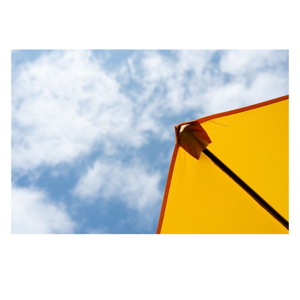 A bright yellow corner of an umbrella or tent stretches diagonally across the upper right, set against a blue sky with soft, scattered white clouds.