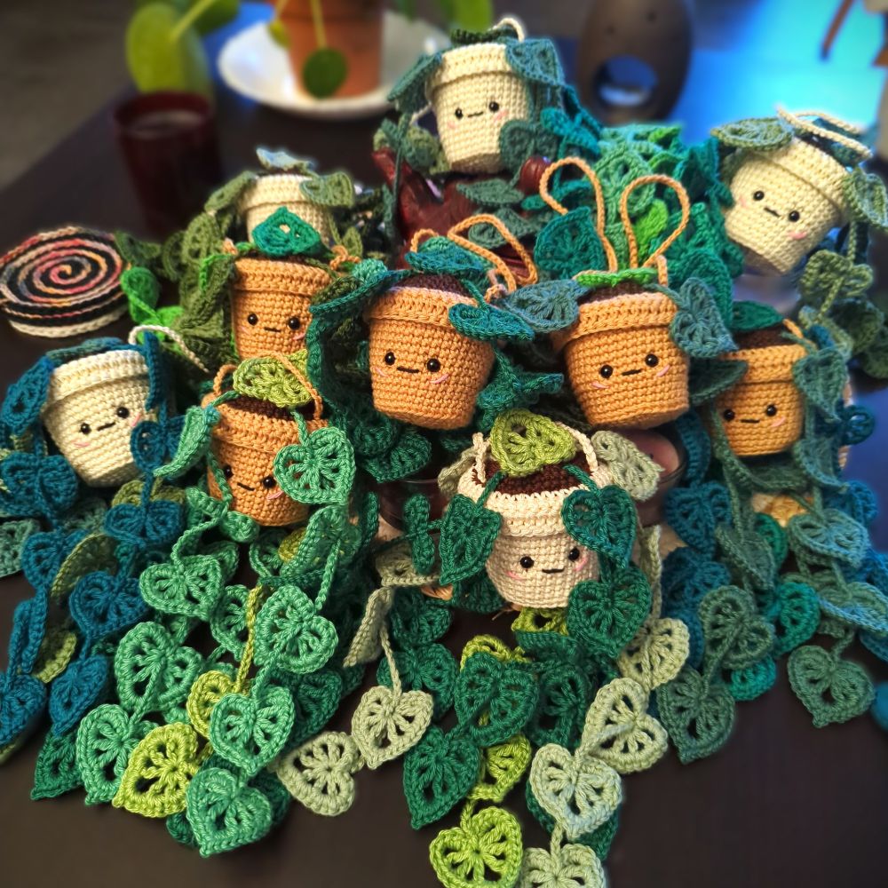 Groupe d'amigurumis plantes suspendues avec des pots blanc crème ou caramel et des feuilles multicolores vertes tous posés sur une table.