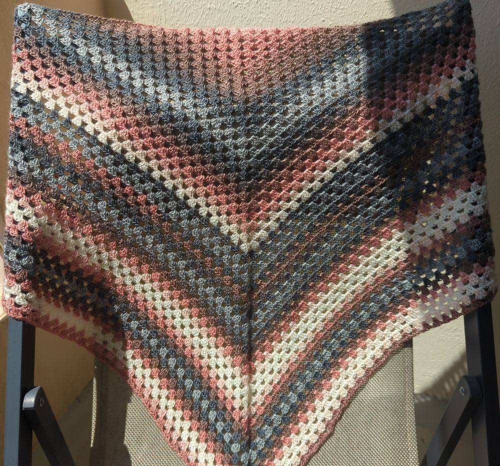 Châle triangle fait au crochet, coloris vieux rose, gris et crème, posé sur le dossier d'un fauteuil