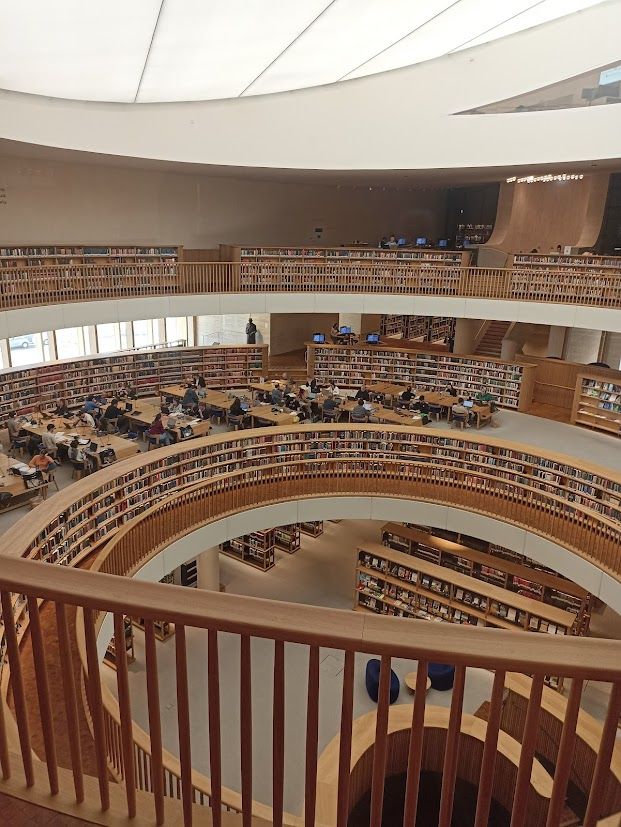 מבט מלמעלה על אולם קריאה בספריה הלאומית: מדפי ספרים בצורת מעגל כשבתוך המעגל אפשר לראות את אולם הקריאה שבקומה מתחת, ומחוץ למעגל שורה של שולחנות מוארכים, ומאחוריהם עוד מדפי ספרים