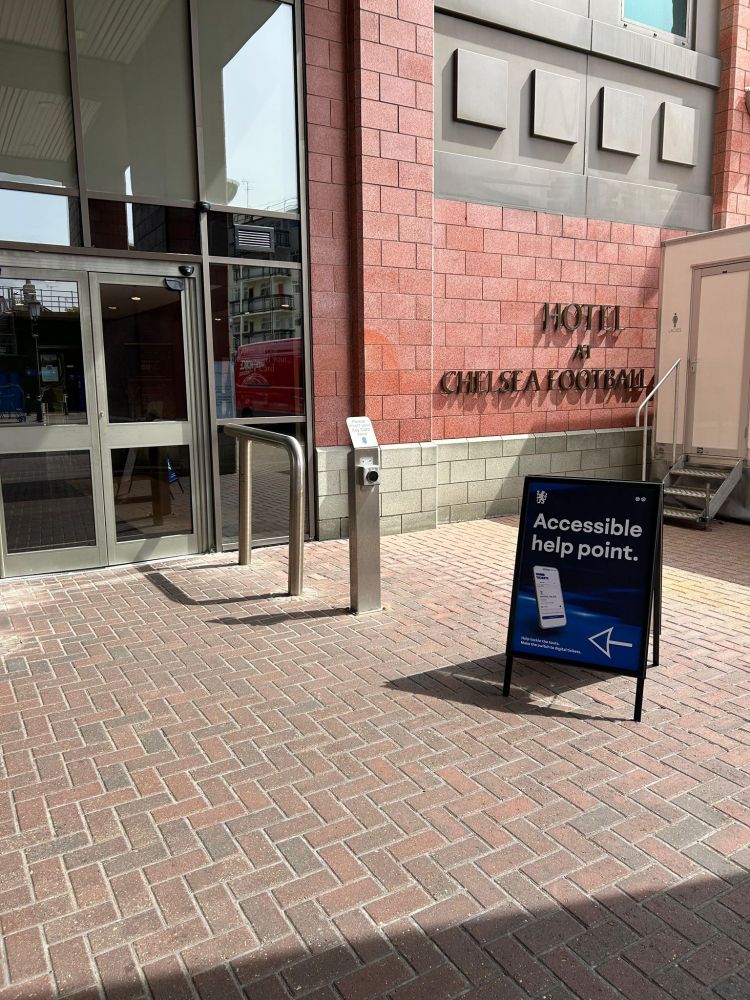 Image description: A sign with the text "Accessible help point" stands outside the entrance of a hotel at Stamford Bridge.