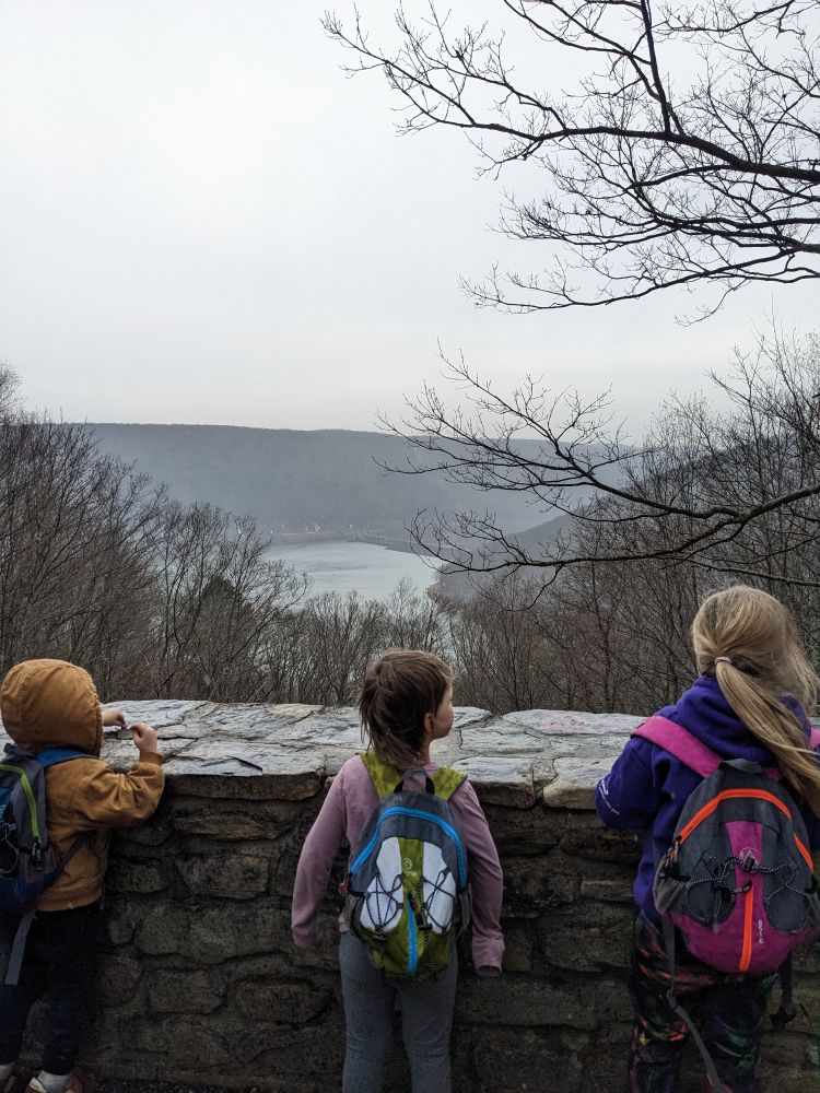 three kids looking over a stone overlook at a dam in the rain