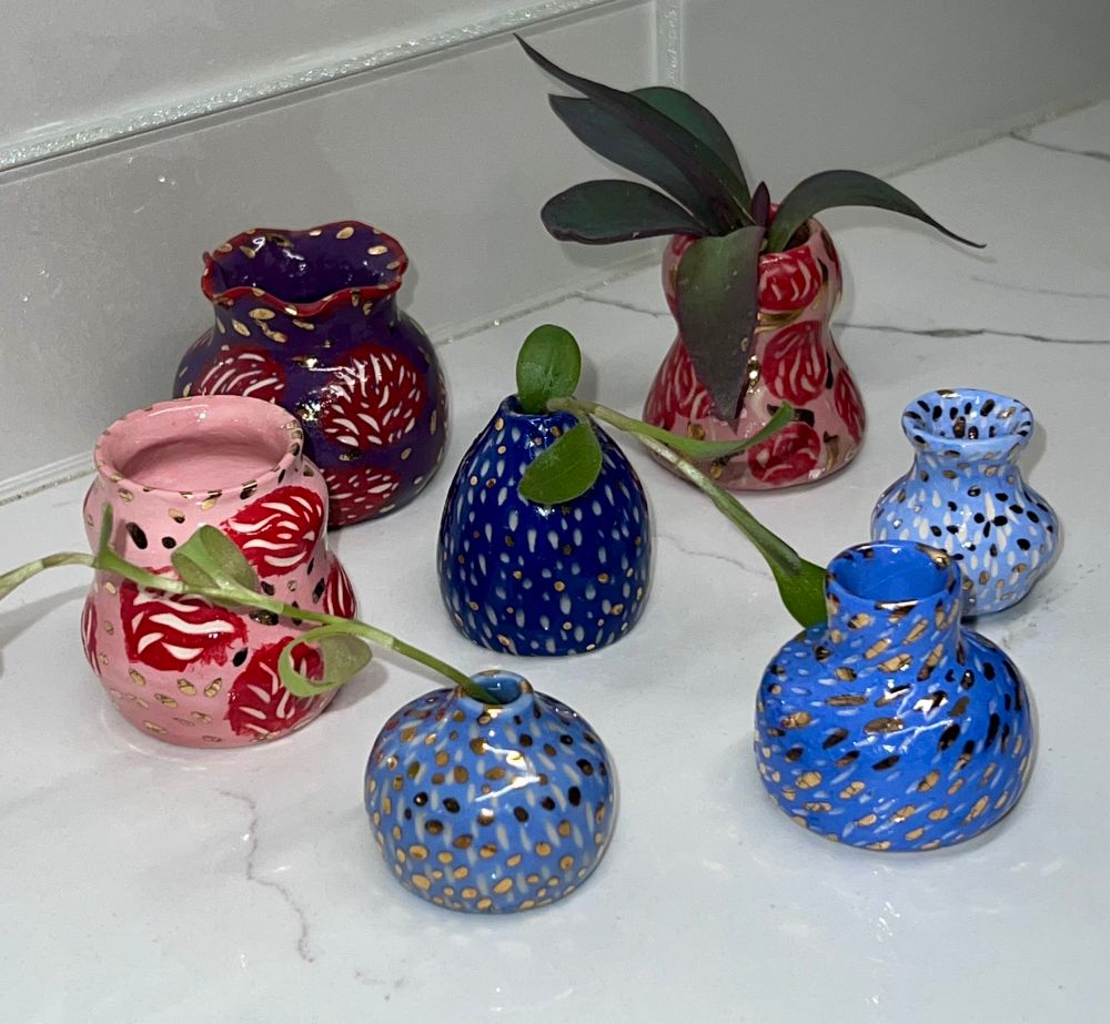 Set of seven miniature vases a various shapes and heights, featuring sgraffito abstract design, in shades of blues, pinks, red and purple gloss glazes, all finished with 22 karat gold metallic glaze accents. 