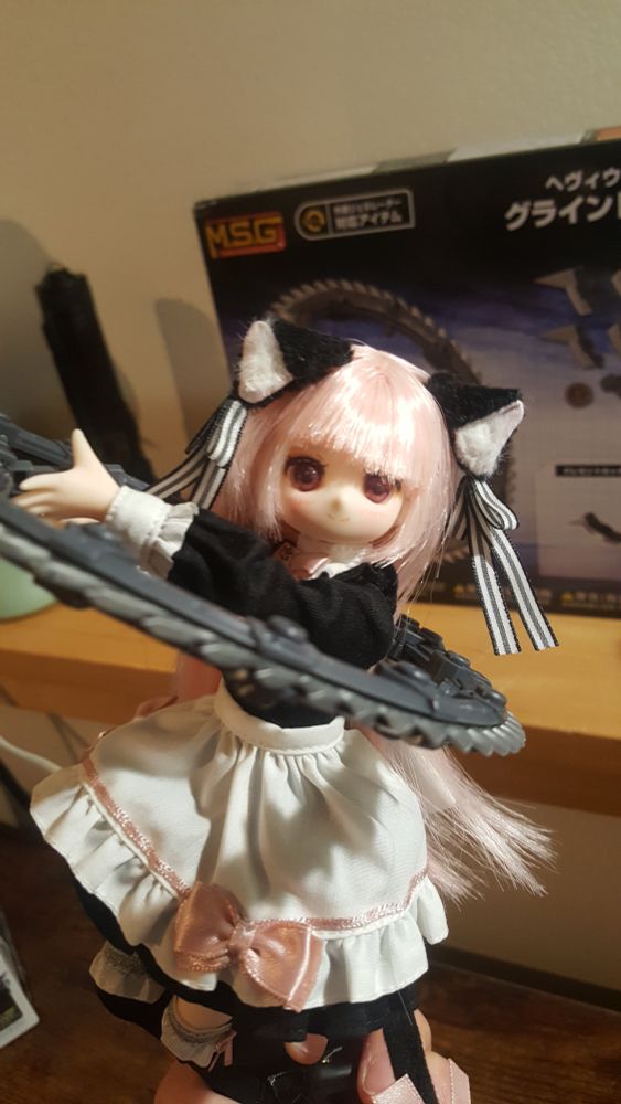 a pink haired cat girl doll wearing a maid outfit is holding a large grindsaw in the shape of a circle and staring at the viewer