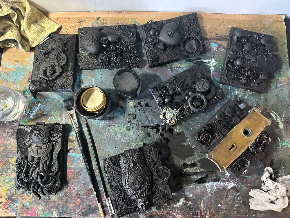 Messy desk overhead shot with 8 mixed media paintings in black 