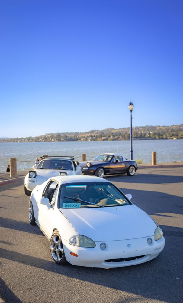 Two Miatas and a Del Sol parked near the water