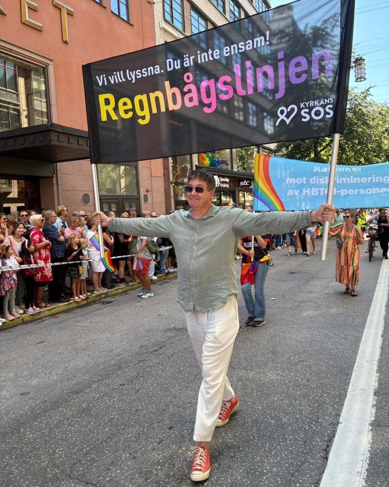 Jag med en banderoll där det står: ”Vi vill lyssna. Du är inte ensam!”
Sedan i större stil: ”Regnbågslinjen”.
Och längst ner till höger loggan för Kyrkans SOS.