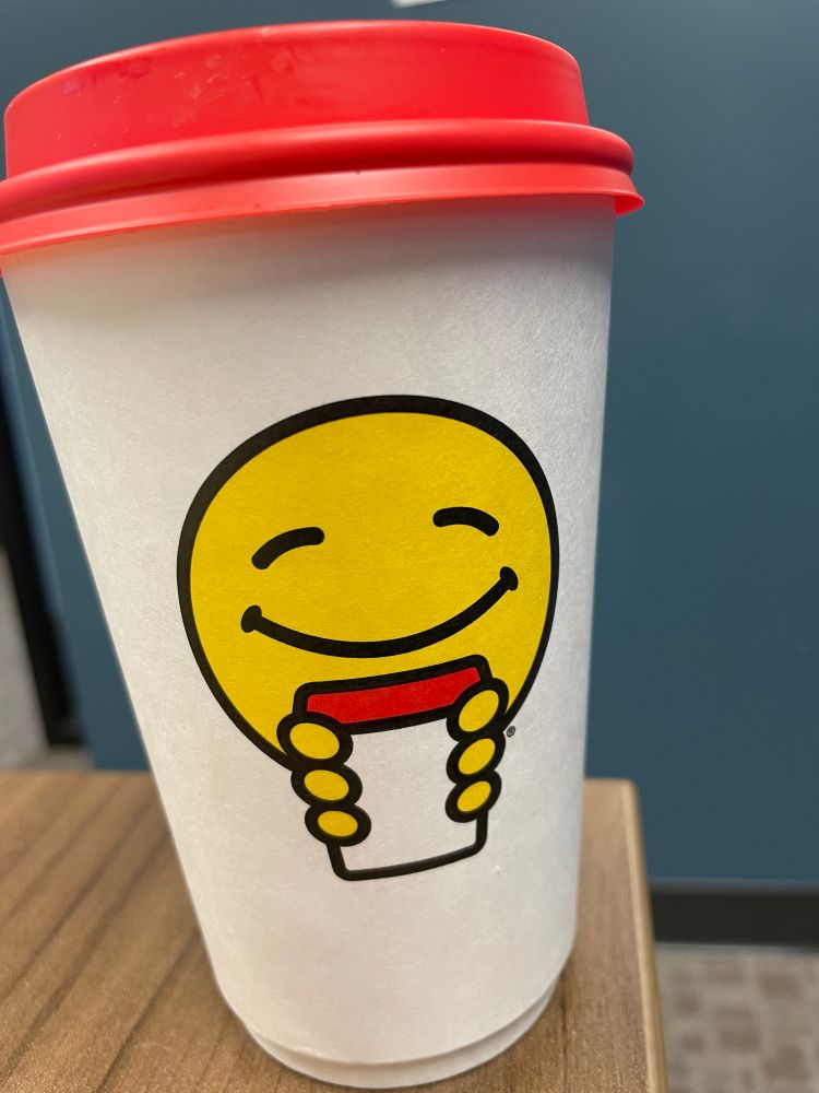 Paper cup of Scooter’s coffee with a little yellow smiley face holding a little coffee cup. 