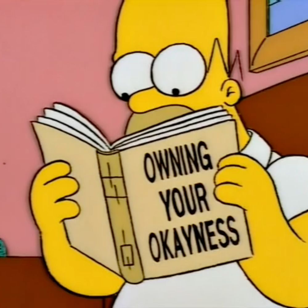 Homer Simpson holding a book that reads “Owning your Okayness”