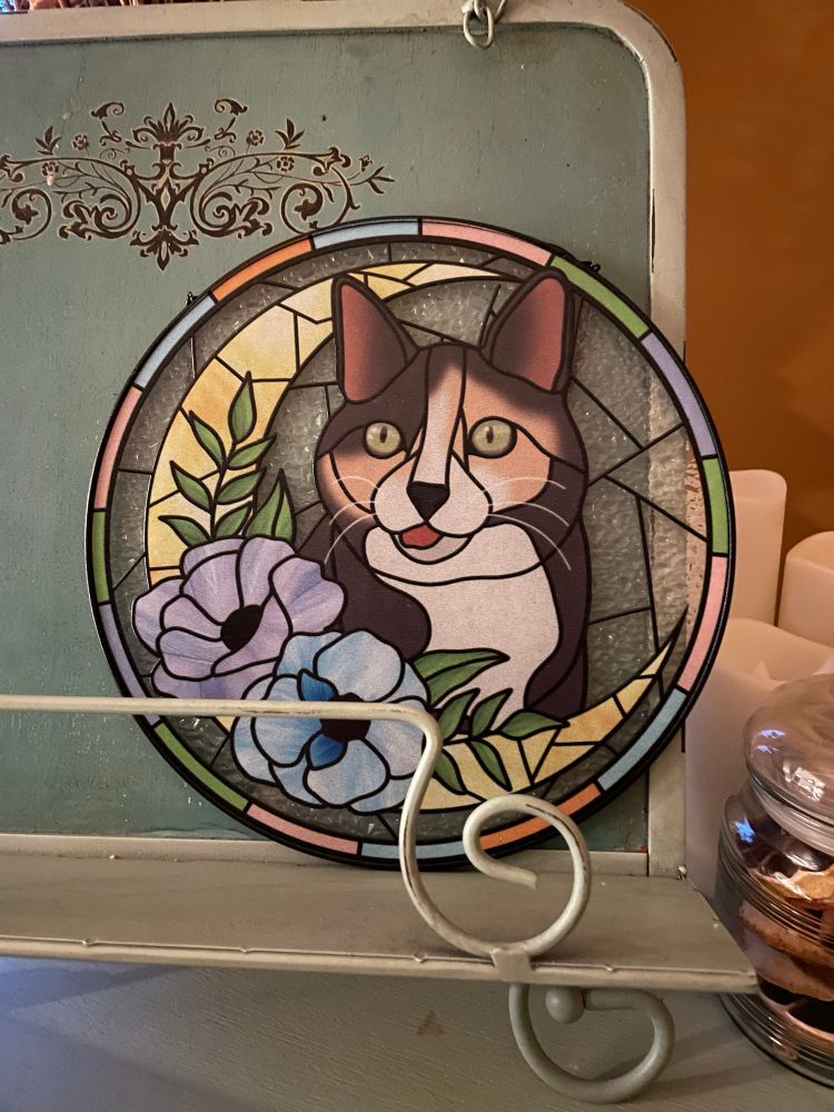 a stained glass piece my friend Leila got me for christmas showing my cat Chihiro with her tongue sticking out. she’s framed with a crescent moon and blue flowers