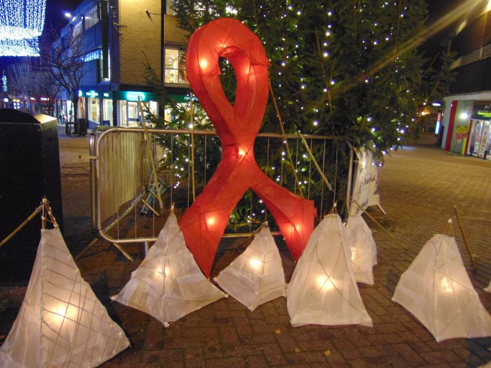 A large paper red ribbon, surrounded by triangular lanterns, in front of a small Christmas tree